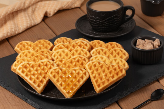 Delicious heart-shaped waffles served with coffee and sugar on a wooden table in a cozy setting