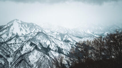 Obraz premium Skiers enjoy the slopes of Gala Yuzawa with stunning views of Ishiuchi Maruyama and Yuzawa Kogen in Niigata, Japan. Snow-covered mountains and a small town stretch across a scenic winter valley.