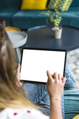Femme assise confortablement dans un intérieur moderne, tenant une tablette numérique avec un écran blanc. Scène de détente en journée, avec lumière naturelle, et doigt qui clique	