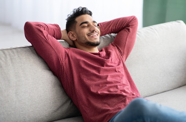 Happy middle-eastern guy in casual chilling at home, reclining on couch with closed eyes and...