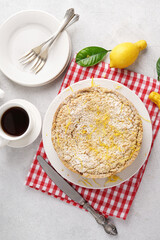 Homemade Italian lemon pie with streusel on light table with cut piece and cup of coffee, red napkin, top vertical view