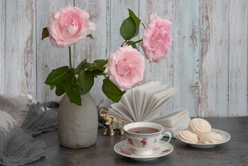 A beautiful soft pink bouquet of roses on a table next to a cup of tea and marshmallows.