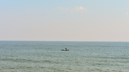 Lone fisherman on a small boat in calm sea under a clear sky at Bay of Bengal.