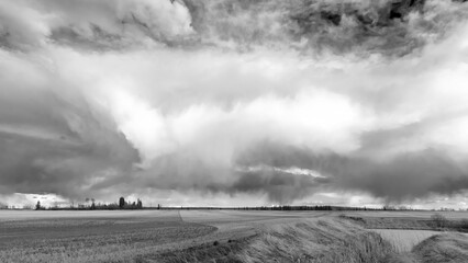 A monochrome scenic rural landscape capturing a freshly seeded agricultural field under a dramatic...