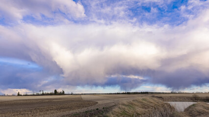 A scenic rural landscape capturing a freshly seeded agricultural field under a dramatic cloudy spring sky, raining in the horizon.