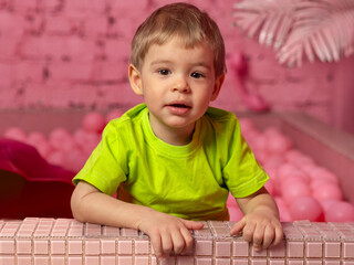 2 year old boy wearing a green t-shirt on a pink background.