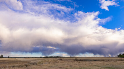 A scenic rural landscape capturing a freshly seeded agricultural field under a dramatic cloudy spring sky, raining in the horizon.