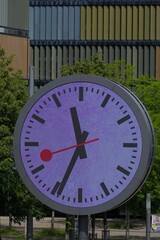 Iconic round clock face, vibrant purple hues, and classic black hands against lush greenery. A symbol of precision and timeless design in an urban setting.