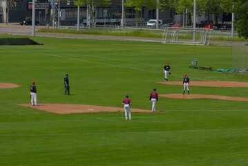 An expansive green field hosts a baseball game, capturing the sport's anticipation and strategic play under a bright, open sky.