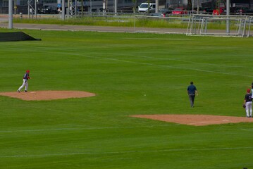 An expansive green field hosts a baseball game, capturing the sport's anticipation and strategic play under a bright, open sky.