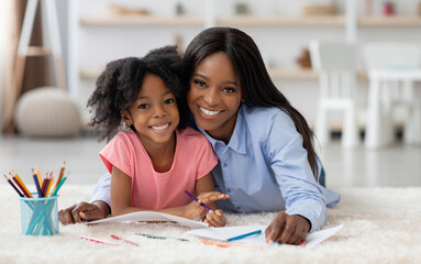 Portrait of cheerful loving african american mom and little girl with bushy hair daughter coloring...
