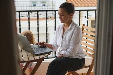 Woman Working on Laptop at Outdoor Balcony With Child Nearby