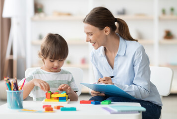 Early kids development. Cute little boy playing logical geometry game, positive woman specialist...