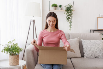 Online store and purchase delivery. Smiling girl received good order in living room interior in...