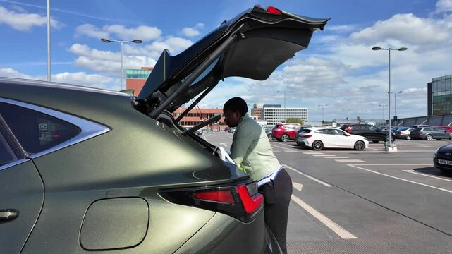 Hampshire England UK. 28.05.2025. Video.  African woman loading shopping into car boot in a supermarket car park.