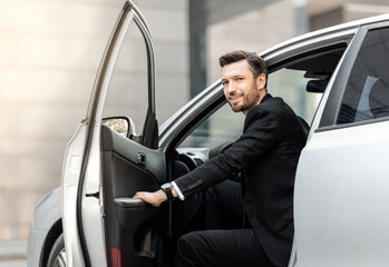 Successful middle-aged entrepreneur getting in expensive car, driving to airport, side view....