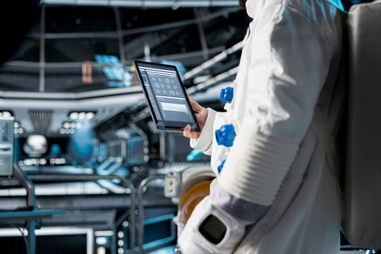 Close up of astronaut using tablet to view spacecraft analytics during scientific mission. Spaceship crew member in spacesuit looking at orbital navigation data on device during planetary exploration