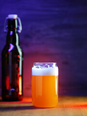 Craft beer glass on table with beer bottle. Neon color background. Copy space