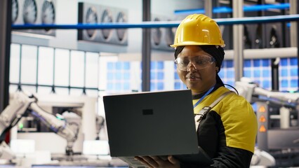 Woman working in industry 4.0 plant using notebook, following maintenance procedures. Smart factory staff member analyzing data on laptop to predict gear failures, camera B