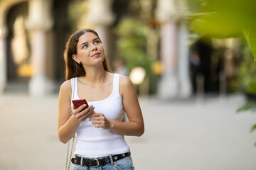 Young smiling girl with phone walks along city street, walks from work to home. Pedestrian in...