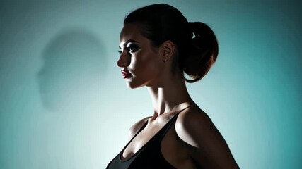 Profile of a Woman: A woman with dark hair in a bun, wearing a black top, is captured in profile against a muted teal backdrop. - Powered by Adobe