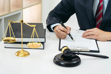 A male lawyer or notary working with contract papers, book and wooden gavel on table in courtroom,...