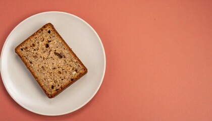 マットなクレイレッドの背景に映えるニュートラルカラーの皿にのったバナナブレッドの一切れが左下に配置された落ち着いた写真

