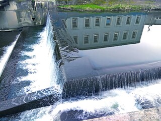 Reflection of architecture in the mirror of the water surface. Movement of the river in the urban development. River dam. Postcard. Cover. Wallpaper