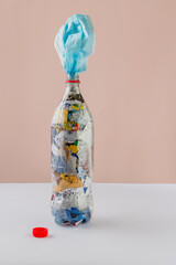 PET bottle filled with plastic waste and wrappers. Face mask inserted on neck of bottle. Red cap.