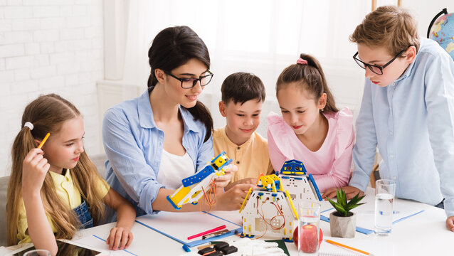 Little technicians working together with teacher in robotics class, creating diy robot