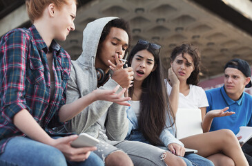 Black teen guy smoking cigarette, his friends judging him. Social issues between young people © Prostock-studio