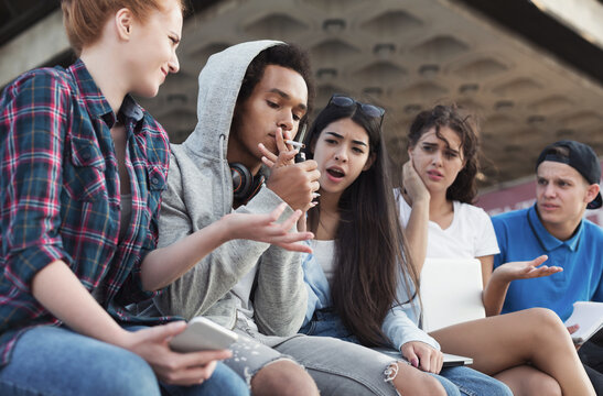 Black teen guy smoking cigarette, his friends judging him. Social issues between young people