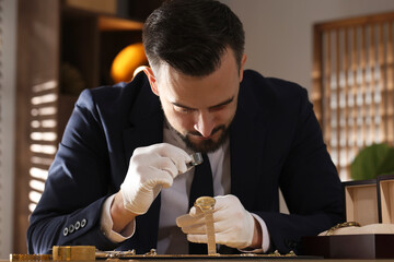 Appraiser with loupe evaluating luxury wristwatch at table indoors