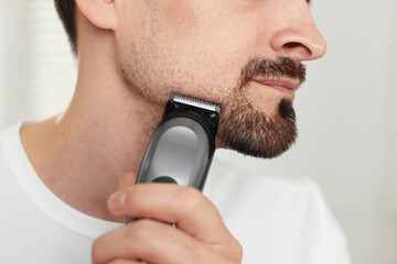 Man shaving with trimmer at home, closeup