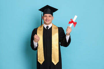 Happy student with diploma after graduation on light blue background