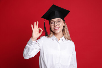 Happy student showing ok gesture after graduation on red background
