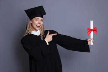 Happy student pointing at diploma after graduation on grey background
