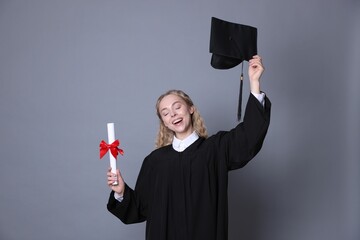 Happy student with diploma and mortarboard after graduation on grey background