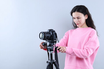 Woman with professional video camera on light grey background, space for text