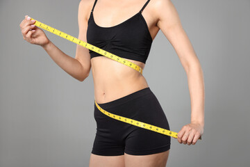 Woman with slim body and measuring tape on gray background, closeup