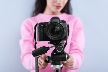 Woman with professional video camera on light grey background, selective focus