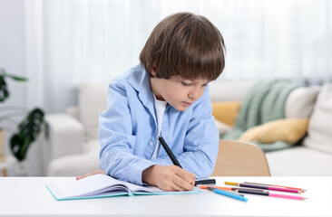 Naklejka premium Cute little boy doing homework at table indoors