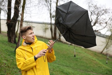 Man with broken umbrella fighting wind under rain outdoors