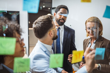 Coworkers brainstorming and planning use sticky notes on glass wall