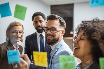 Coworkers brainstorming and planning use sticky notes on glass wall