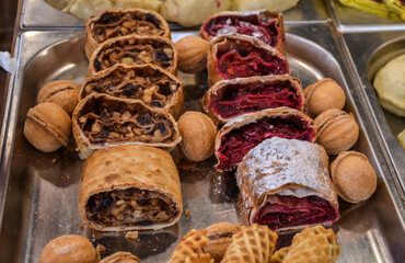 Selection of freshly baked pastries including fruit and nut-filled strudels on a metal tray,...