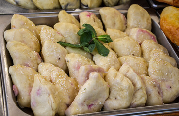 Tray is filled with numerous dumplings with cherries garnished with sesame, accompanied by a mint...