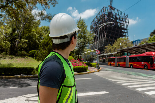 Ingeniero mirando construcci&oacute;n de estructura met&aacute;lica industrial al aire libre con casco blanco y chaleco verde en la ciudad de M&eacute;xico 