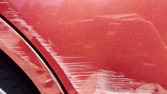 Deep scratches on red metallic car fender showing damage to paint layer and visible abrasion along wheel arch.