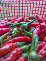 A collection of vibrant red and green chili peppers fills a basket with a checkered pattern background